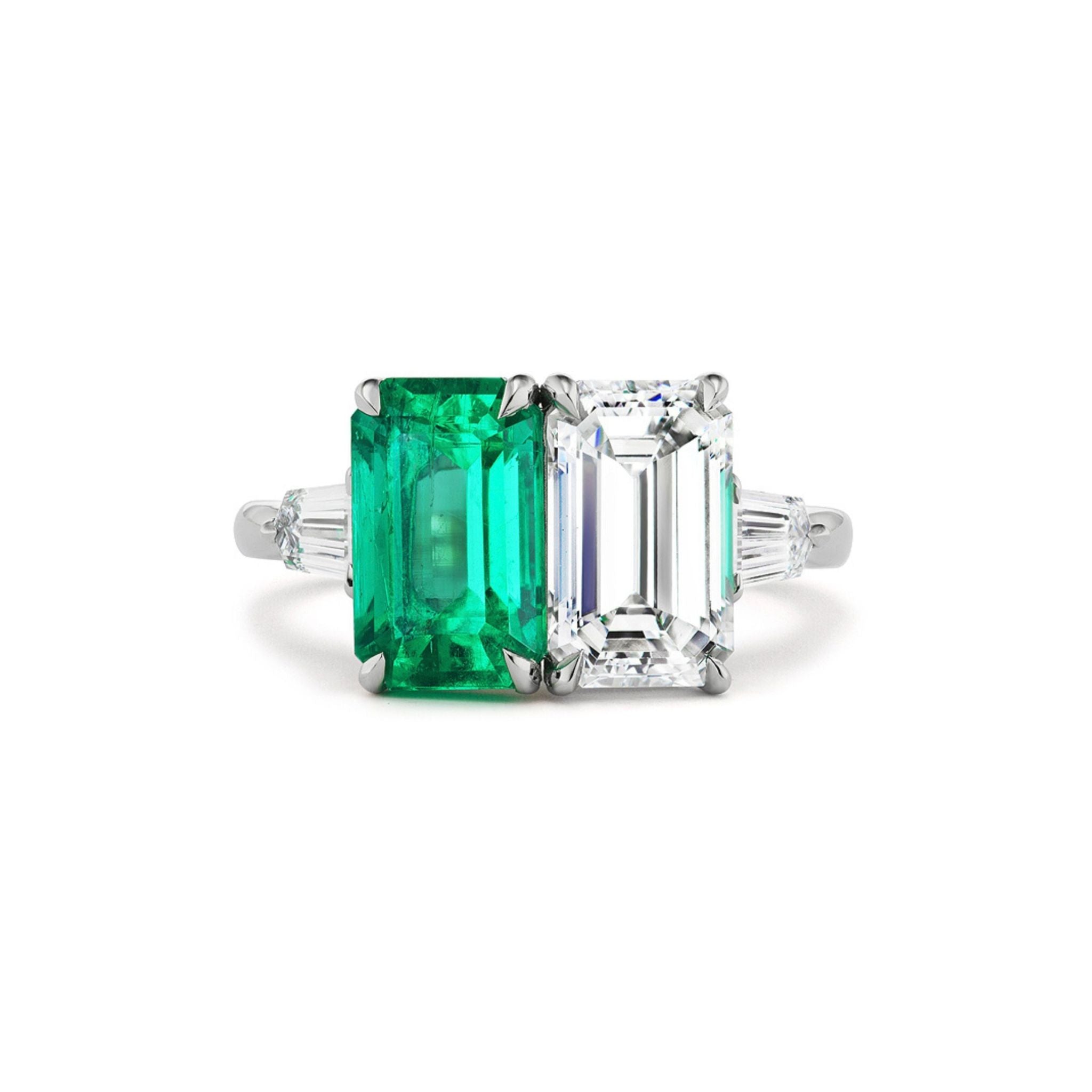 Introducing the Toi et Moi Ring with Emerald Cut Diamond and Emerald: a stunning bespoke engagement ring showcasing two emerald-cut stones—one vivid green emerald and one sparkling diamond—set side by side on a silver band, elegantly accented with tapered baguette diamonds on each side.