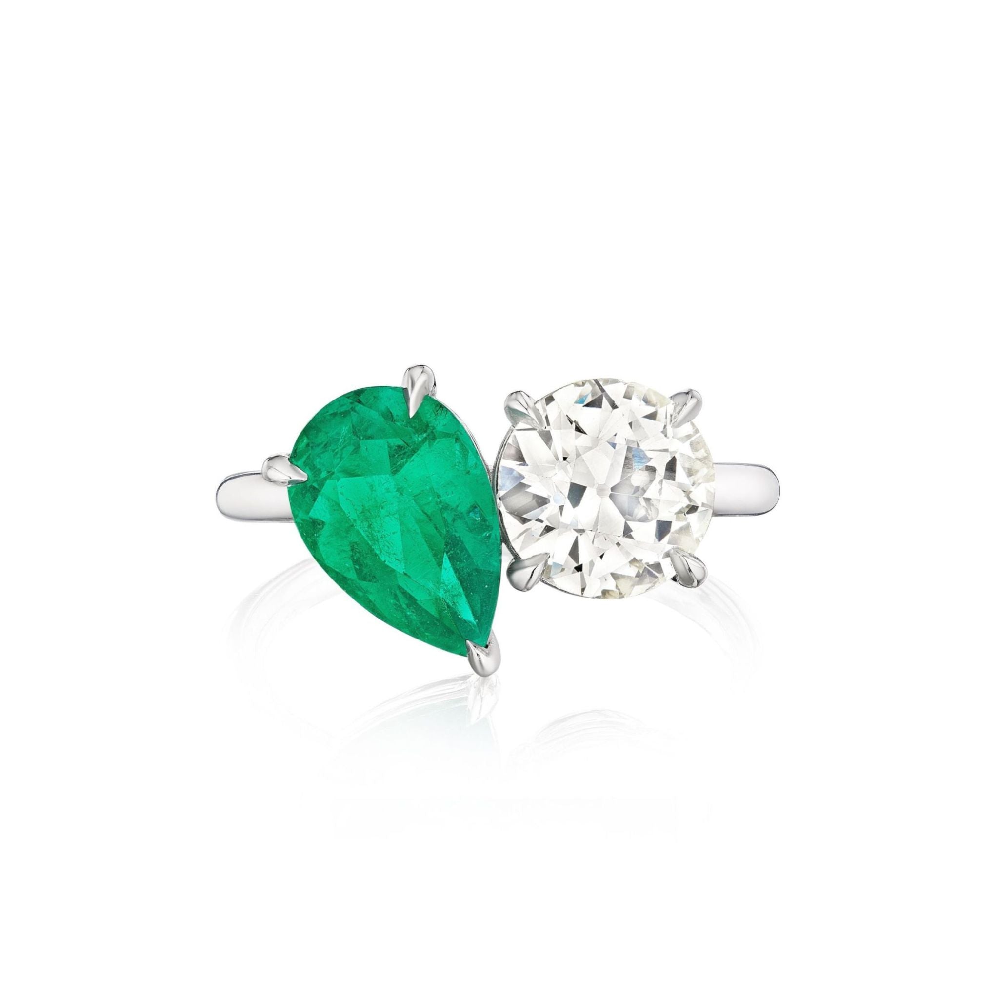The Toi et Moi Pear Shape Emerald and Round Diamond Engagement Ring in White Gold features a striking silver band that displays a pear-shaped emerald alongside a round diamond, both elegantly set in prongs against a pristine white gold background.