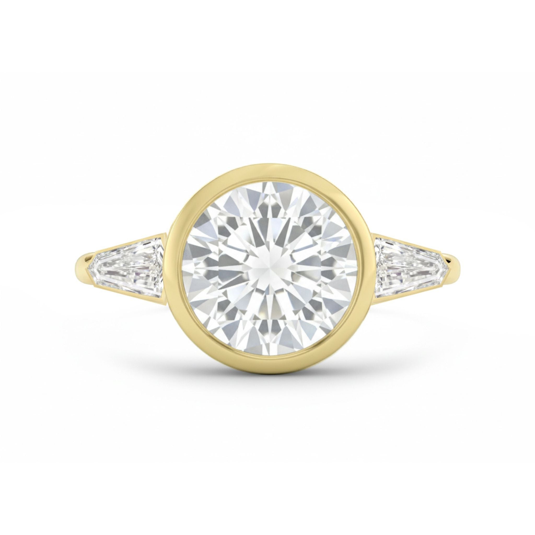 The Bezel Set Round Diamond Engagement Ring with Tapered Baguette Side Stones in Yellow Gold features a bold round center diamond in a bezel setting, accented by two tapered baguette diamonds on each side.
