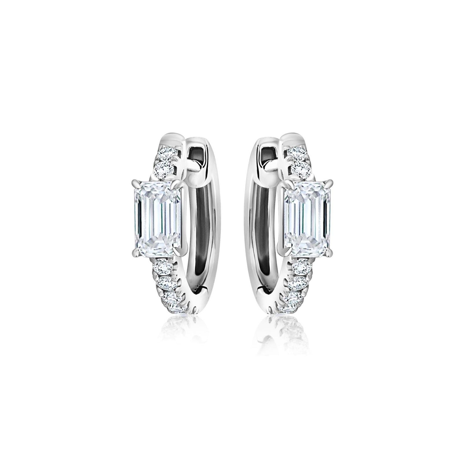 The Pavé Huggie with Emerald Cut Diamonds features silver hoops, each centered with an emerald cut diamond and accented by smaller round gemstones along the front.