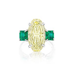 This dazzling Step Cut Oval Yellow Diamond Engagement Ring features a large oval yellow diamond at the center, flanked by square emerald side stones, all set in an elegant 18K white gold band.