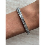 A close-up of a wrist adorned with the Chevron Baguette Diamond Bangle in white gold, featuring a zigzag design and a lustrous finish, captured against a light, textured background.