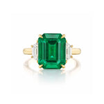 The Emerald Cut Emerald Engagement Ring in Yellow Gold with Trapezoid Baguette Diamond Side Stones showcases a striking emerald-cut emerald centerpiece, complemented by two elegant trapezoid baguette diamonds on either side, all set in 18k yellow gold and beautifully displayed against a white background.
