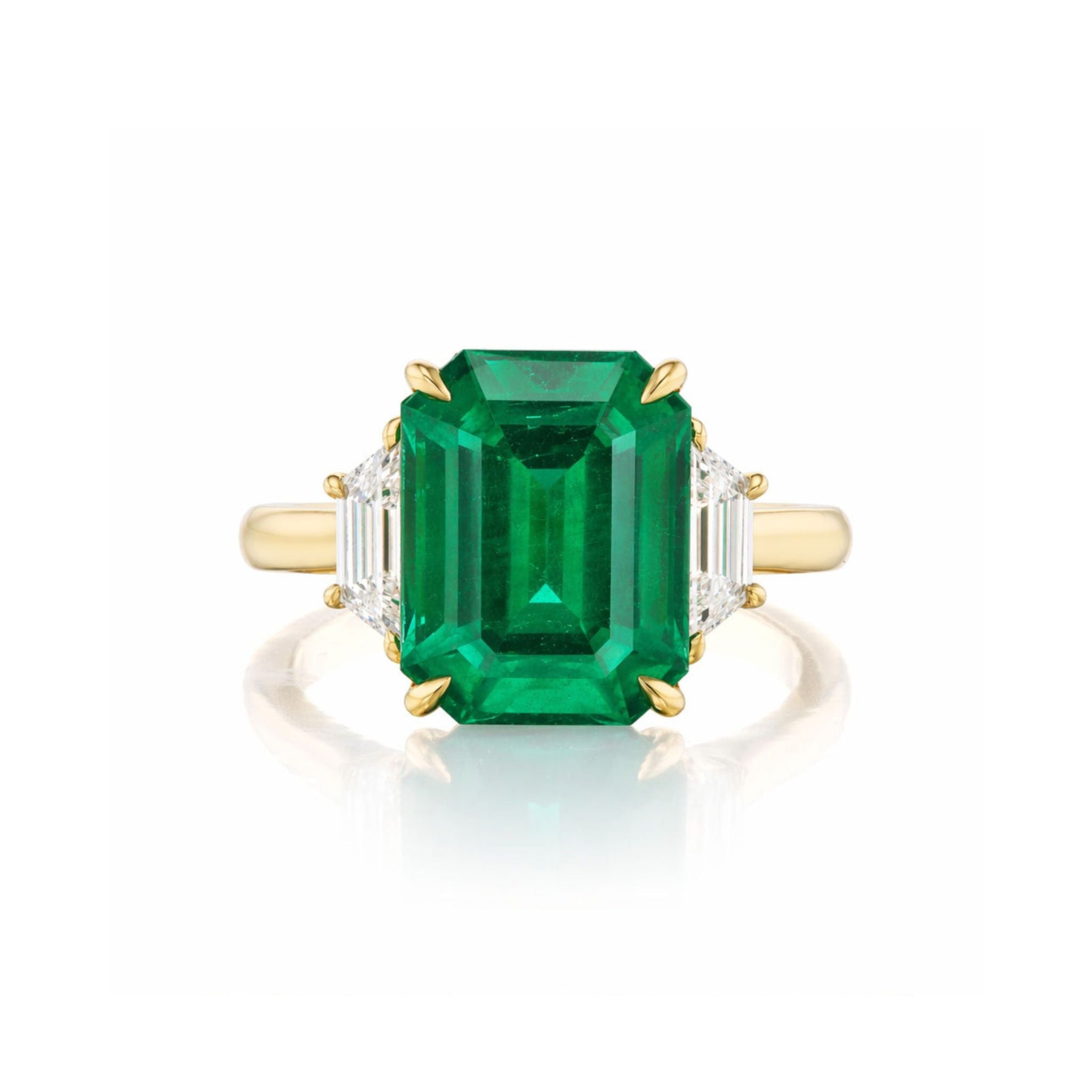 The Emerald Cut Emerald Engagement Ring in Yellow Gold with Trapezoid Baguette Diamond Side Stones showcases a striking emerald-cut emerald centerpiece, complemented by two elegant trapezoid baguette diamonds on either side, all set in 18k yellow gold and beautifully displayed against a white background.