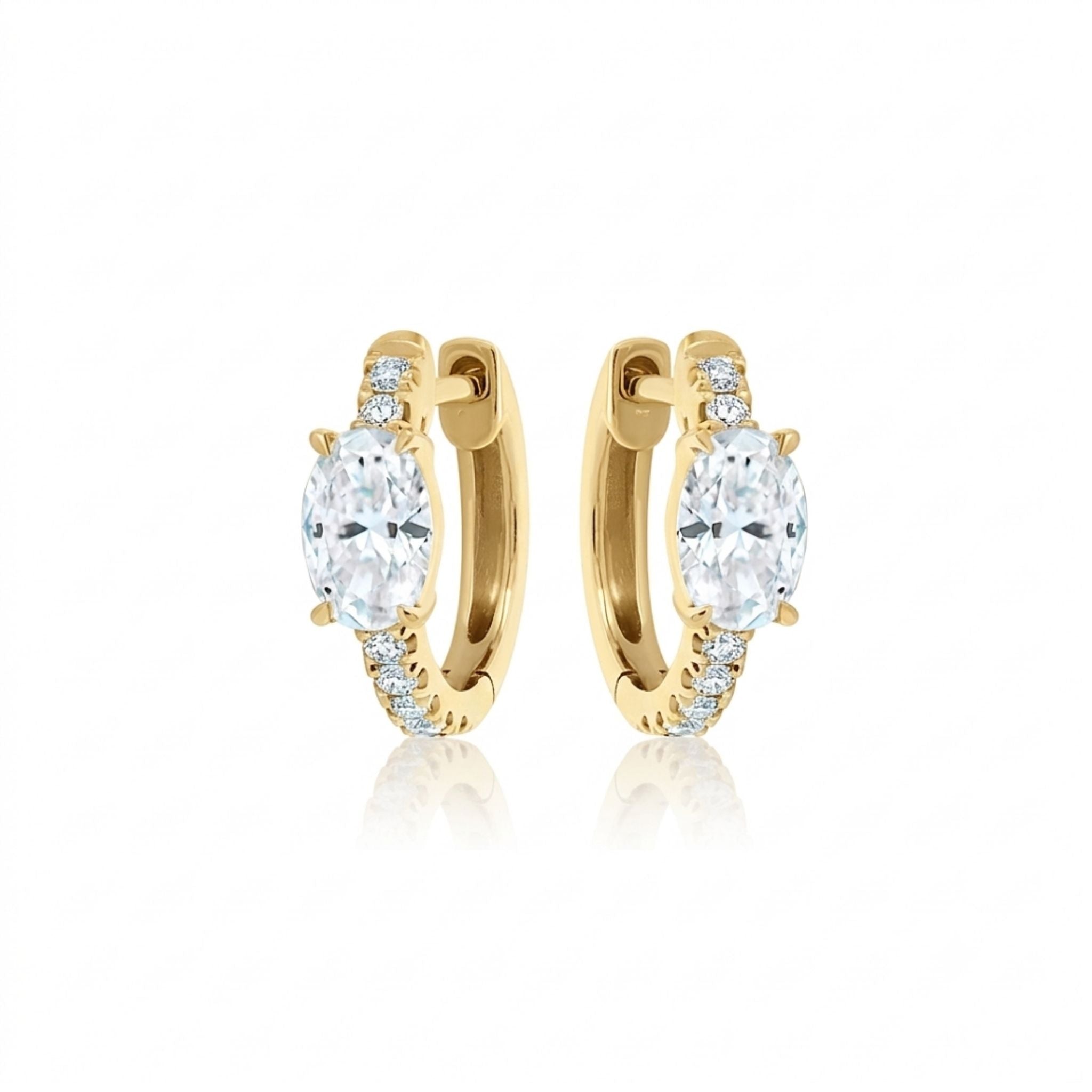 The Pavé Huggies with Oval Shape Diamond are 18k gold hoop earrings showcasing a large oval diamond centerpiece and a pavé row of smaller diamonds along the front, displayed against a white background.