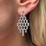 Close-up of a person with light skin and blonde hair wearing Art Deco Chandelier Earrings in white gold, featuring emerald cut diamonds arranged in a geometric grid pattern.