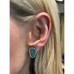 Close-up of a woman's ear with straight blonde hair, wearing Opal Pavé Studs—teardrop-shaped earrings featuring vibrant boulder opals set in white gold and bordered by pavé diamonds.