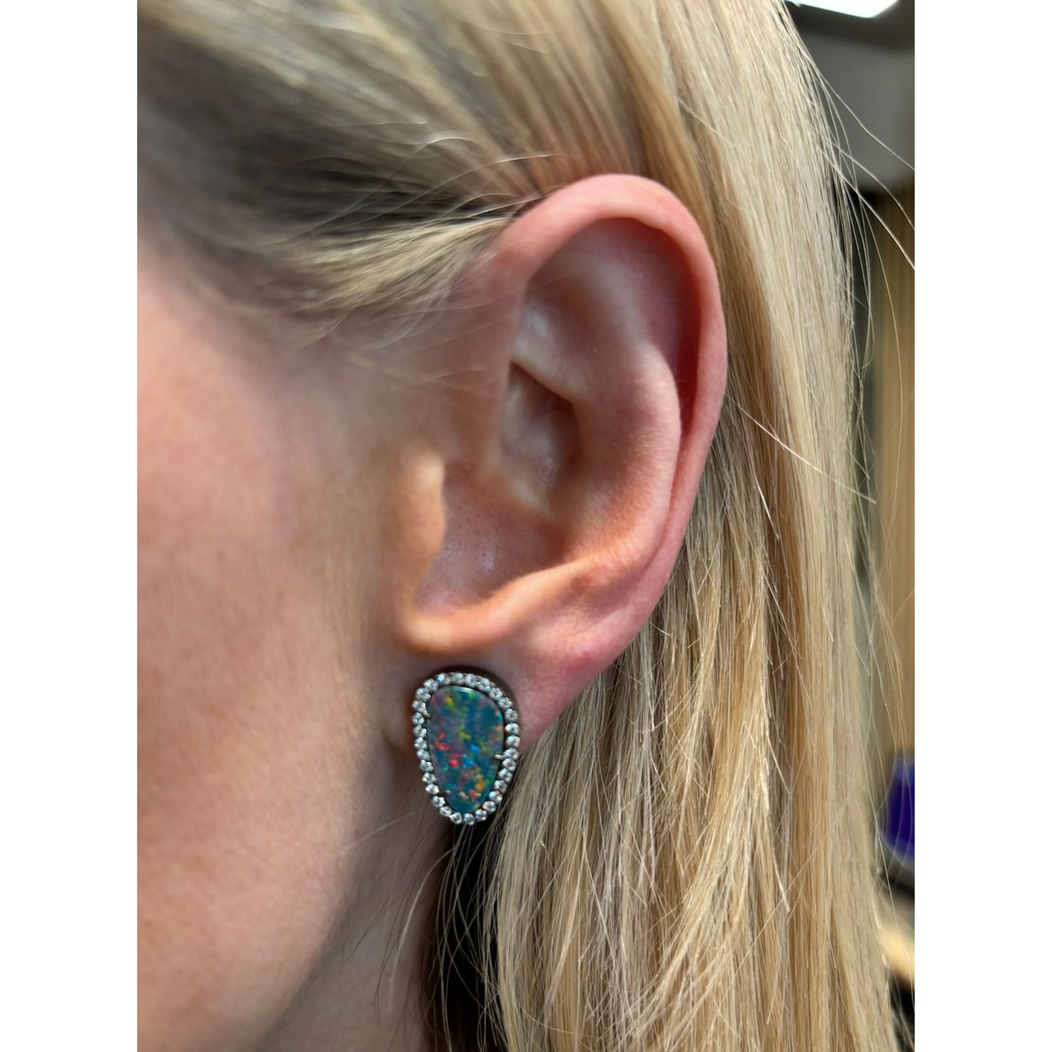 Close-up of a woman's ear with straight blonde hair, wearing Opal Pavé Studs—teardrop-shaped earrings featuring vibrant boulder opals set in white gold and bordered by pavé diamonds.