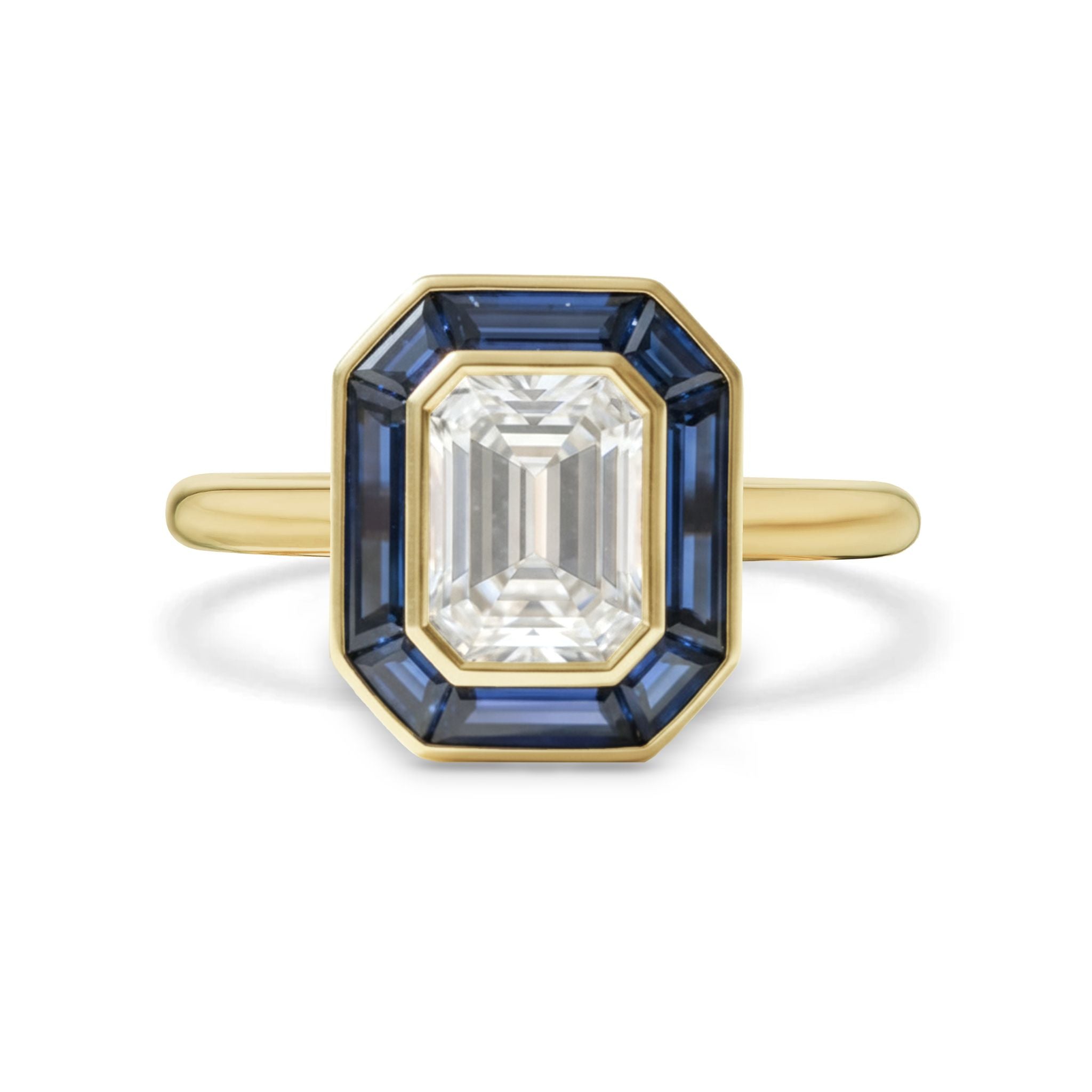 The Mosaic Bezel Set Emerald Cut Diamond Engagement Ring features a geometric bezel setting with a trapezoid blue sapphire halo, all crafted in yellow gold.