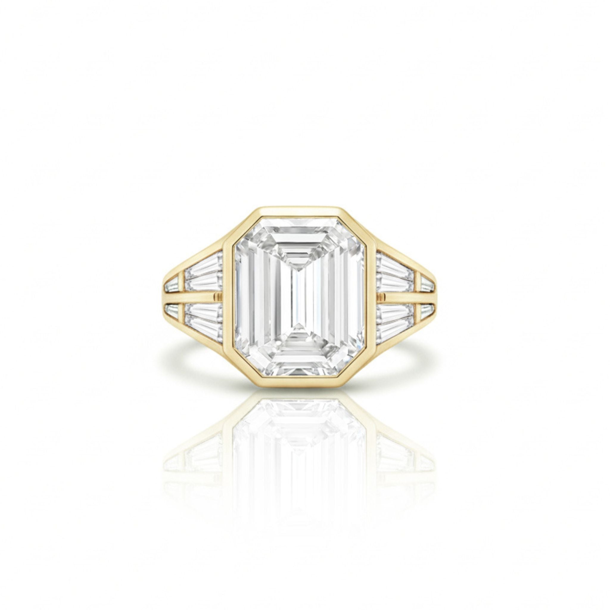 The Bezel Set Emerald Cut Diamond Engagement Ring with Tapered Baguette Side Stones in Yellow Gold is displayed on a white background, featuring a striking emerald-cut center diamond flanked by tapered baguette side stones.