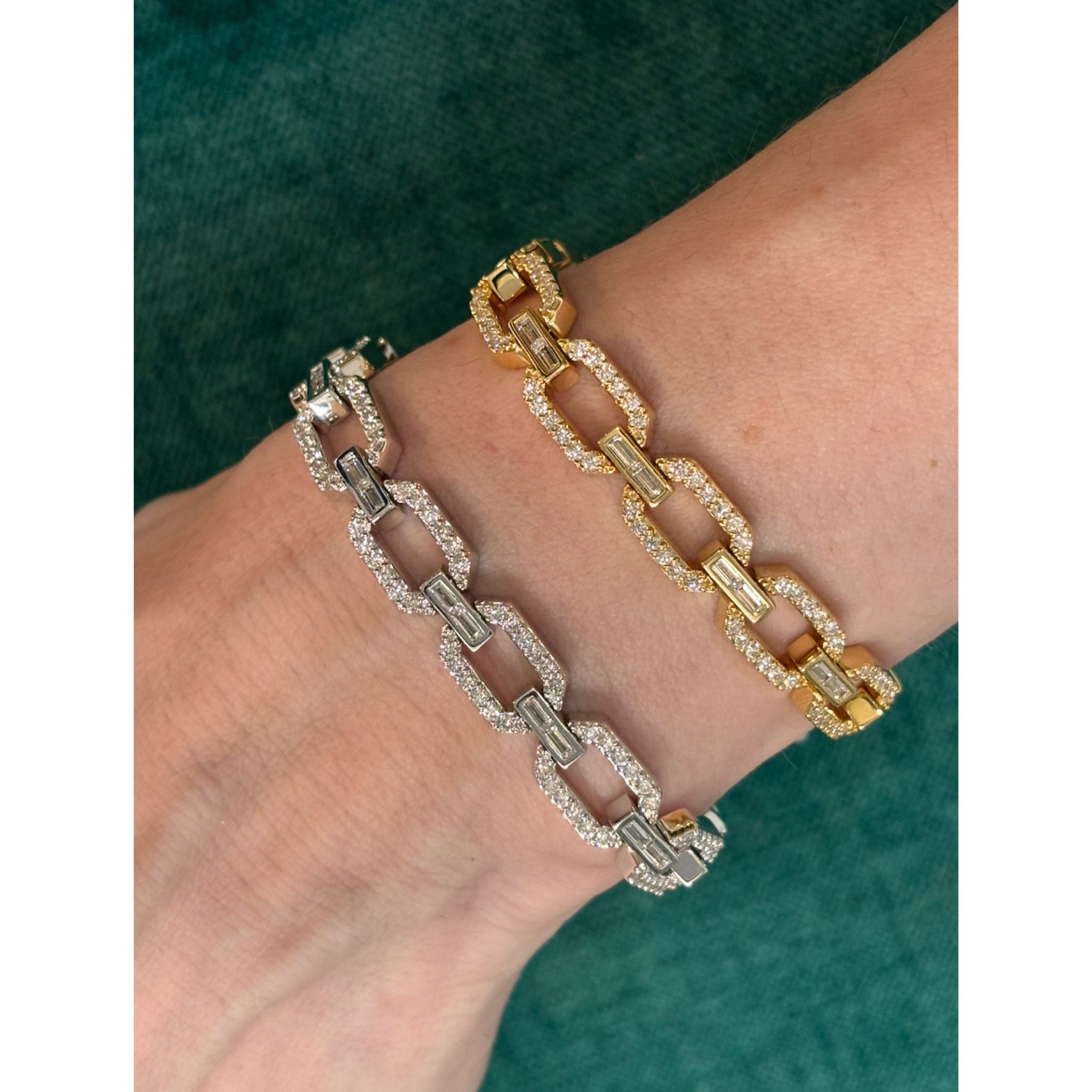 The Bezel Set Baguette Diamond Pavé Chain Bracelet in White Gold, sparkling like diamonds, is worn on a wrist against a textured green background.