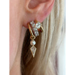 Close-up of an ear with Triple Huggies featuring emerald cut, round, and kite shape diamonds in 18K yellow gold. Light blonde hair appears in the background.