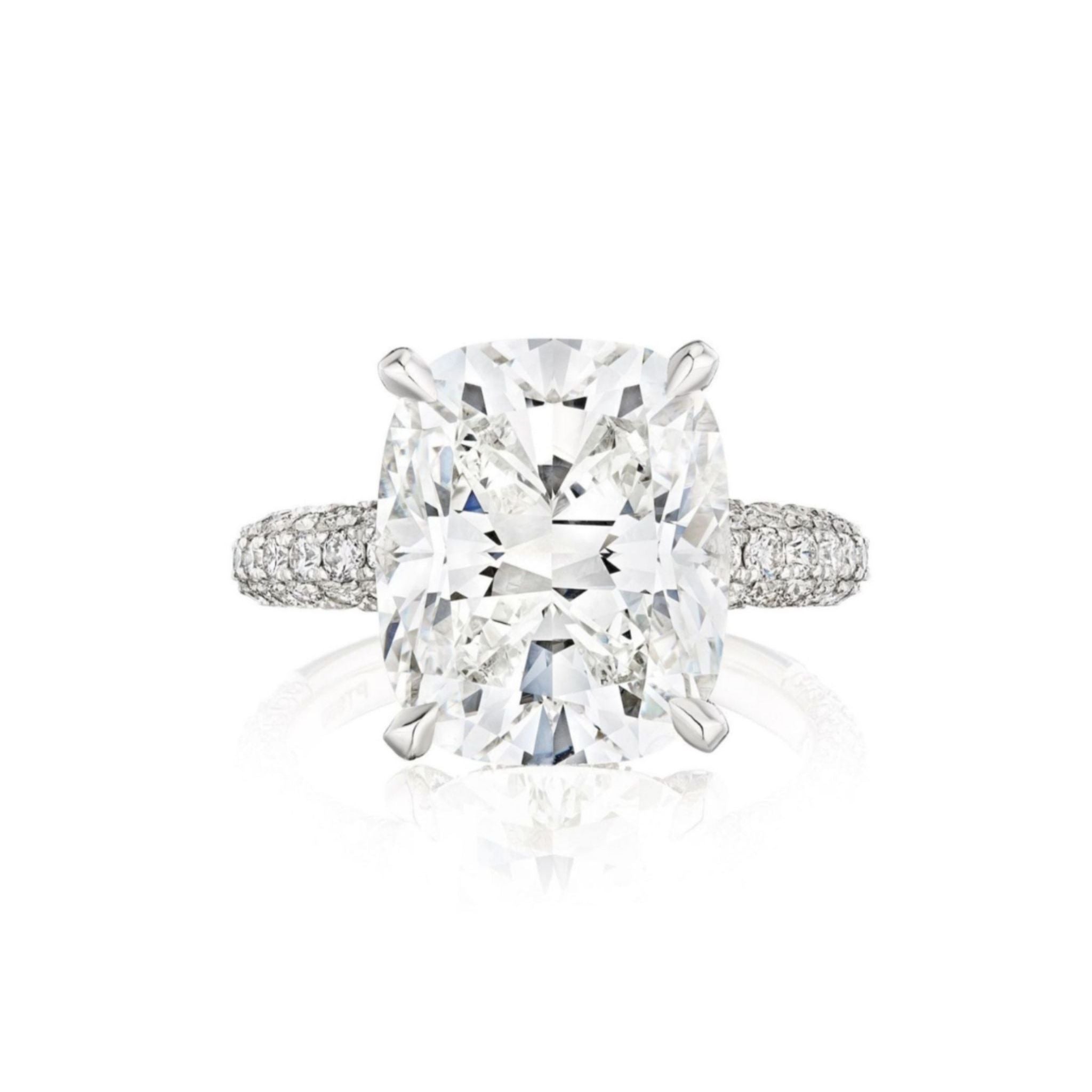 The Cushion Cut Diamond Engagement Ring with Pavé Band features a large center stone secured by four prongs and a pavé band encrusted with small diamonds, beautifully displayed against a white background.