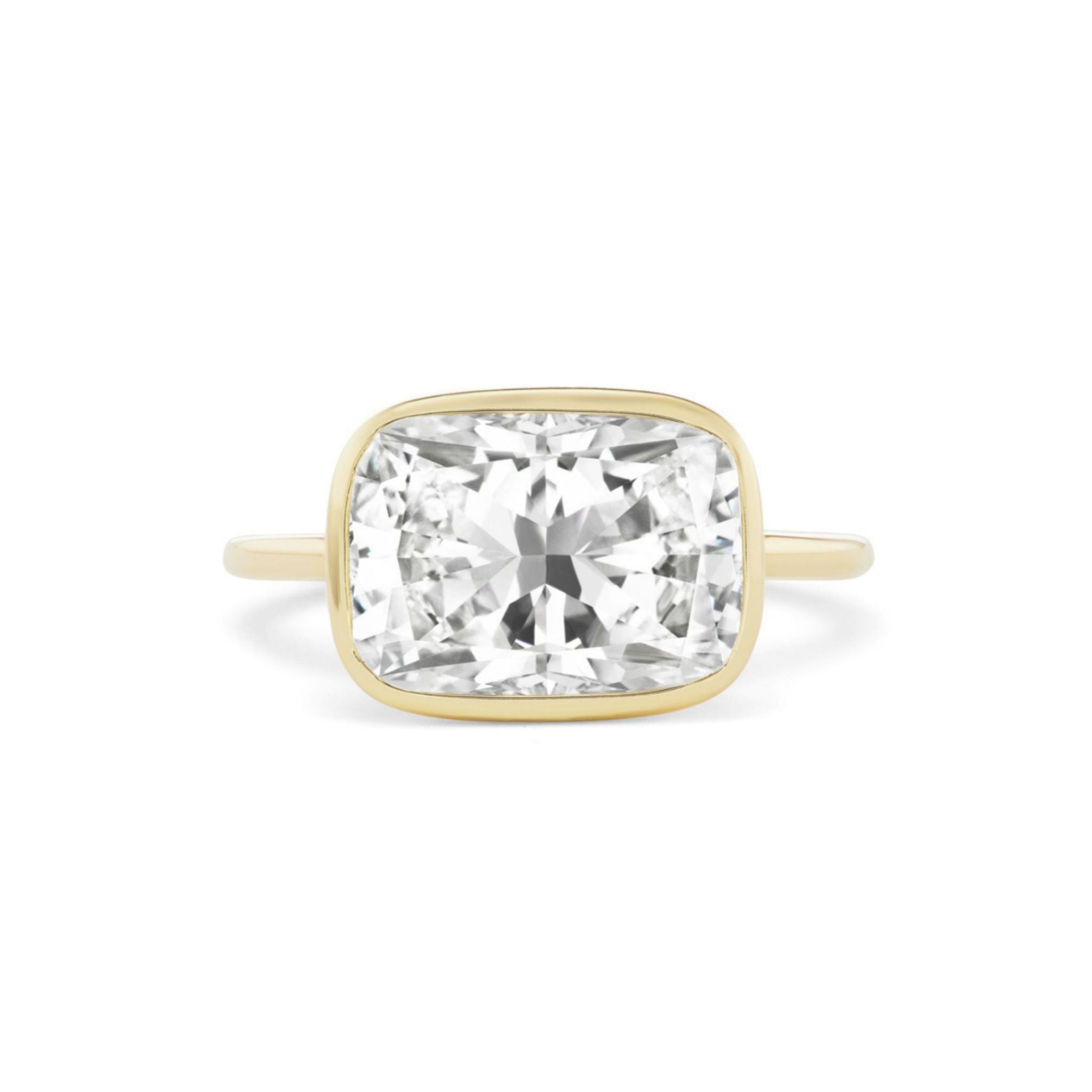 The East-West Bezel Set Cushion Cut Diamond Engagement Ring features a striking cushion-cut diamond set horizontally in a sleek bezel setting, showcased against a white background—a refined and distinctive choice for an engagement ring.