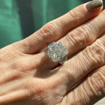 A close-up of a hand with a glittery gold fingernail wearing the Radiant Cut Diamond Engagement Ring with Bezel Set Epaulette Side Stones, set in silver, as sunlight highlights the ring’s sparkling brilliance.