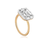 An East-West Collet Setting Emerald Cut Diamond Engagement Ring featuring a large, rectangular emerald-cut diamond set in a silver prong setting on a gold band, displayed against a white background.