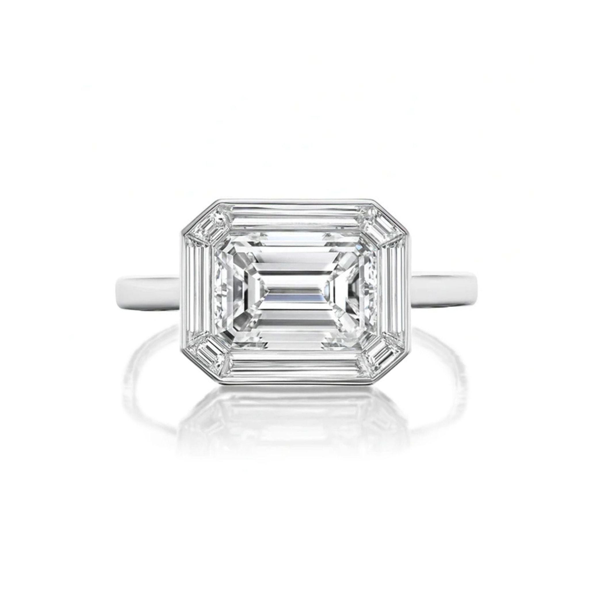 An East-West Set Mosaic Diamond Engagement Ring featuring an emerald-cut diamond with beveled corners, framed by a baguette halo and set on a simple band of white gold or platinum, displayed against a white background.