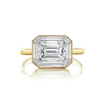 An East-West Set Mosaic Diamond Engagement Ring featuring an emerald-cut diamond surrounded by a baguette halo, elegantly displayed on a simple band and photographed against a white background.