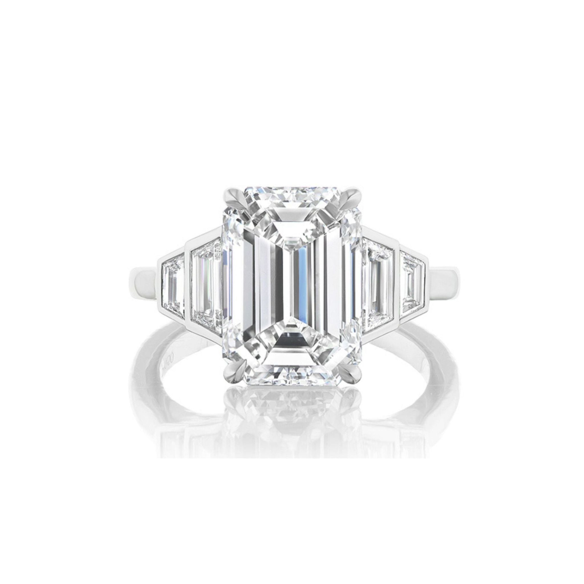 The Echo Emerald Cut Diamond Engagement Ring features a striking emerald-cut center diamond, complemented by bezel-set graduating trapezoid side stones, beautifully displayed on a white background.