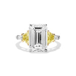 An elegant Emerald Cut Diamond Engagement Ring, featuring a striking emerald-cut clear diamond center, accented by fancy yellow trapezoid and white tapered baguette side stones, all set on a silver band.