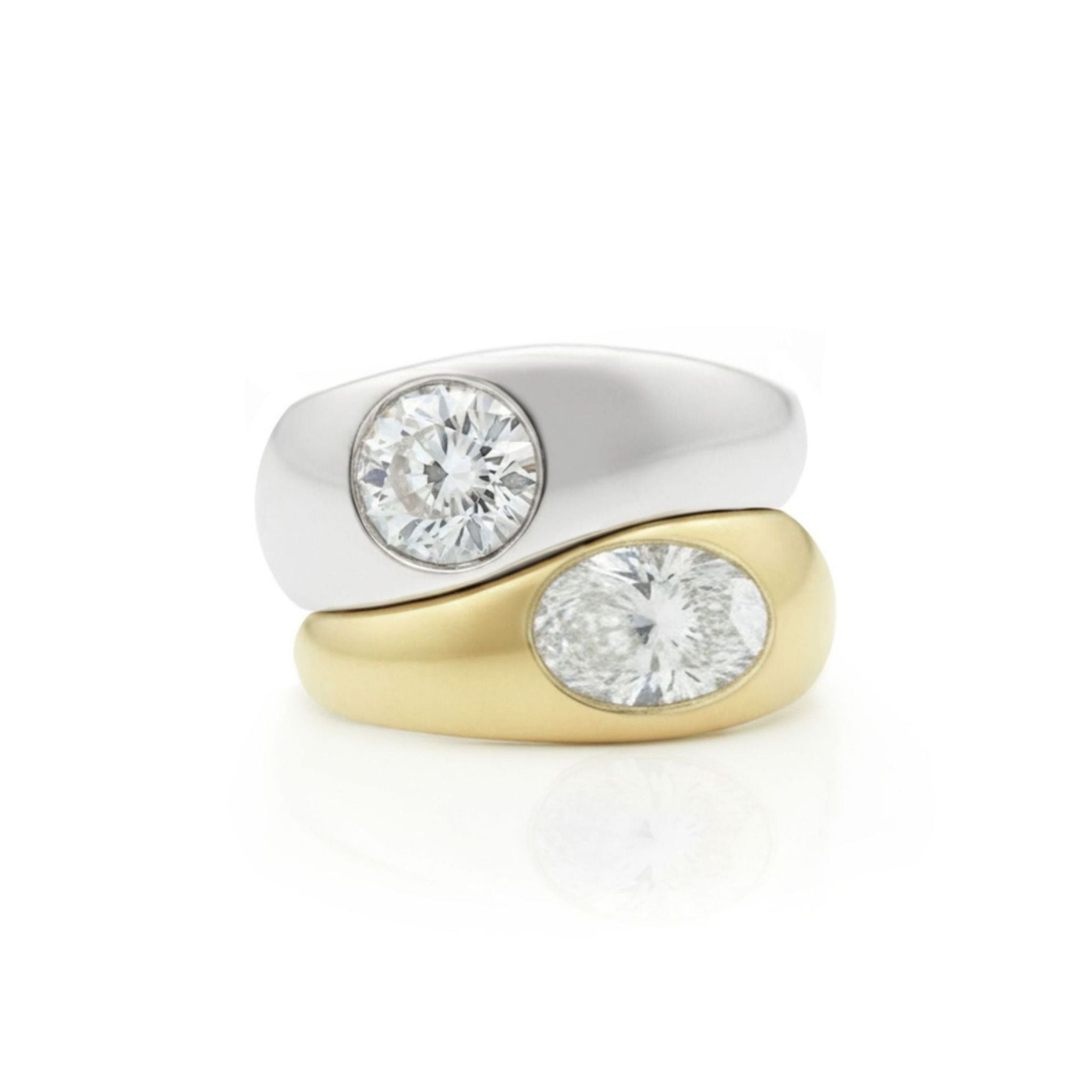 Stacked against a plain white background are two rings: the Stacked Burnish Set Round Diamond in White Gold ring and the Oval Shape Diamond in Yellow Gold Engagement Ring.