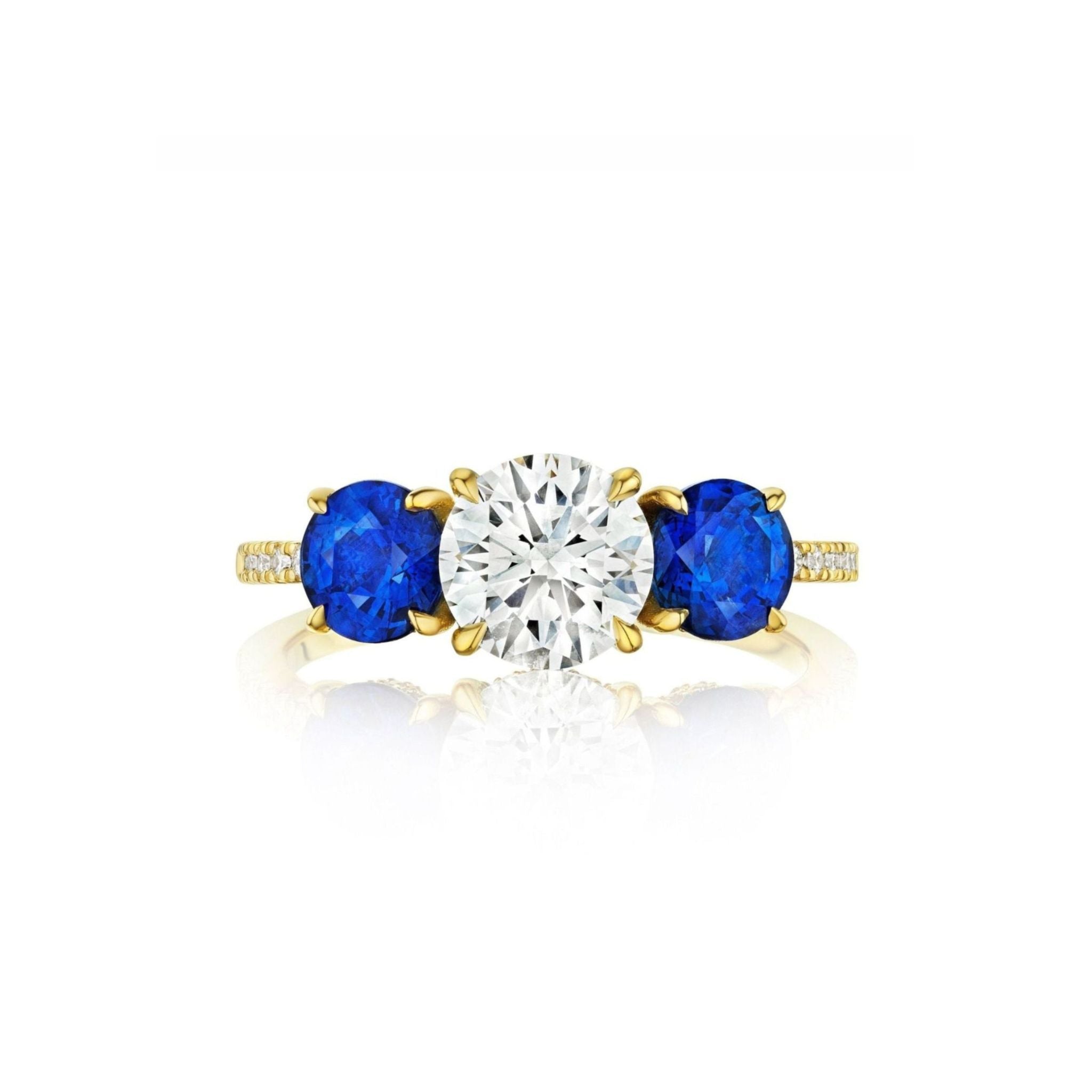 Introducing the Round Diamond Engagement Ring with Round Sapphire Side Stones—crafted in exquisite 18k yellow gold, this stunning ring showcases a large round brilliant diamond at its center, complemented by vibrant blue round sapphire side stones and sparkling accent diamonds set along the band.