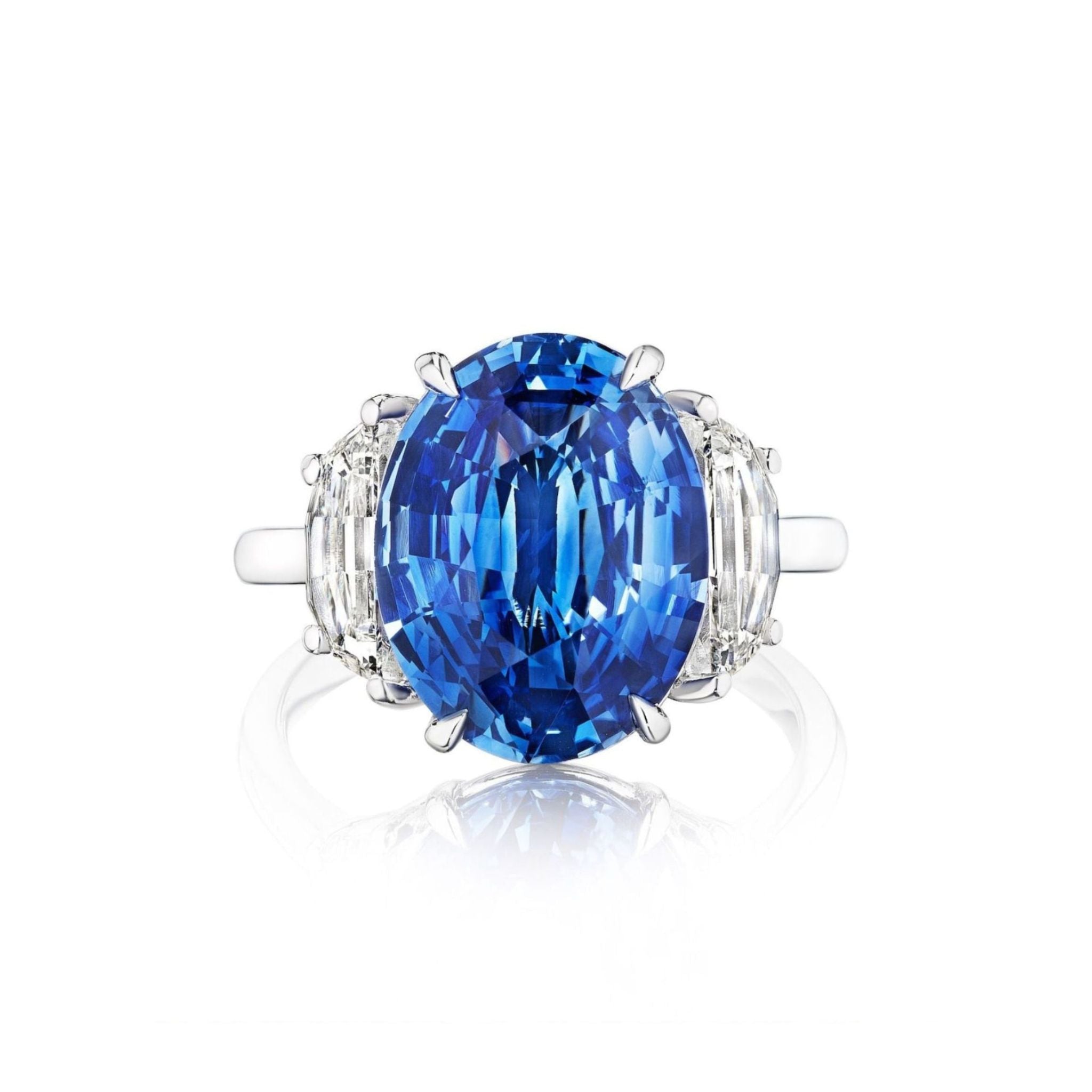 A platinum engagement ring named the "Modified Oval Blue Sapphire Engagement Ring" features a prominent modified oval blue sapphire centerpiece, accented by modified half moon side stones, all set on a simple platinum band.