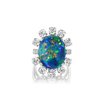 The Sunburst Oval Opal Ring with Round Brilliant Diamonds and Pavé showcases a vibrant oval opal radiating blue, green, and orange hues, encircled by a halo of sparkling diamonds, and is expertly crafted to embody elegance and sophistication.