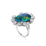 Sunburst Oval Opal Ring with Round Brilliant Diamonds and Pavé: A silver ring showcasing an oval opal gemstone with mesmerizing blue, green, and yellow hues, encircled by a halo of round brilliant diamonds in an elegant pavé setting.