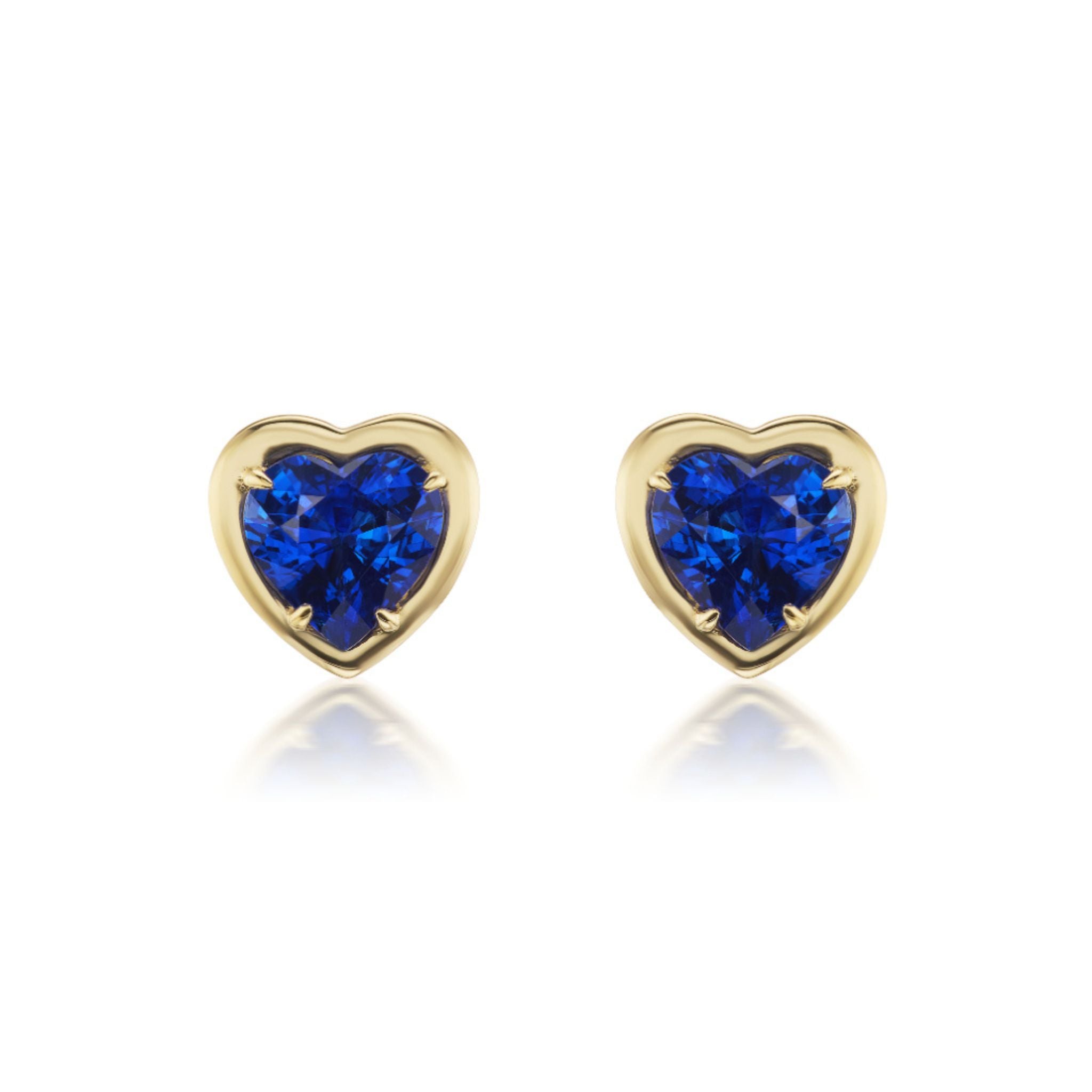 Introducing the Blue Sapphire Heart Studs in Yellow Gold: exquisite 18k yellow gold heart-shaped earrings, each featuring a vibrant blue sapphire at the center, elegantly displayed on a white background with soft reflections for a striking presentation of sapphire jewelry.