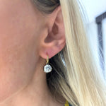 Close-up of a person’s ear wearing a Collet Set Round Diamond Earring in Yellow Gold and Black Rhodium, featuring a large, round diamond pendant. The person's blonde hair is partially visible, and the background is blurred.