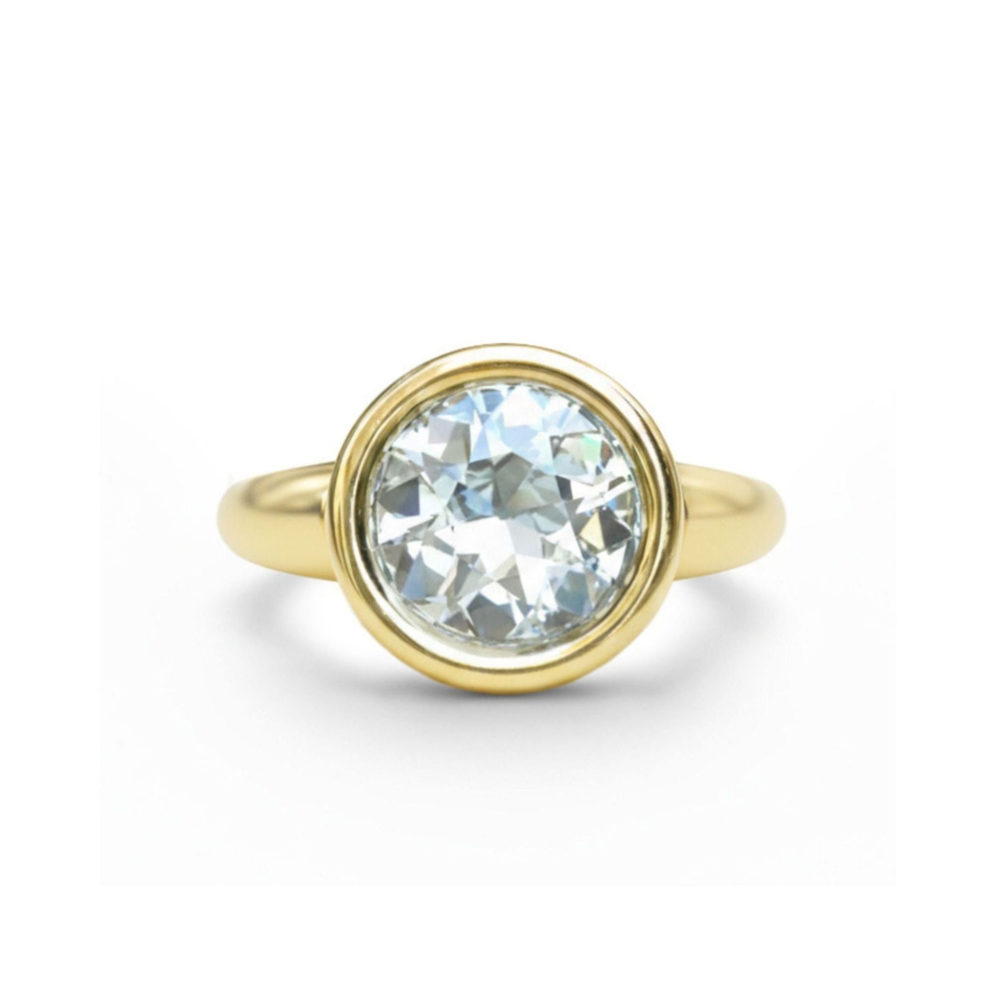 A Bezel Set Round Diamond Engagement Ring in Yellow Gold is displayed against a white background, featuring a round diamond at the center set in a bezel on a simple band.