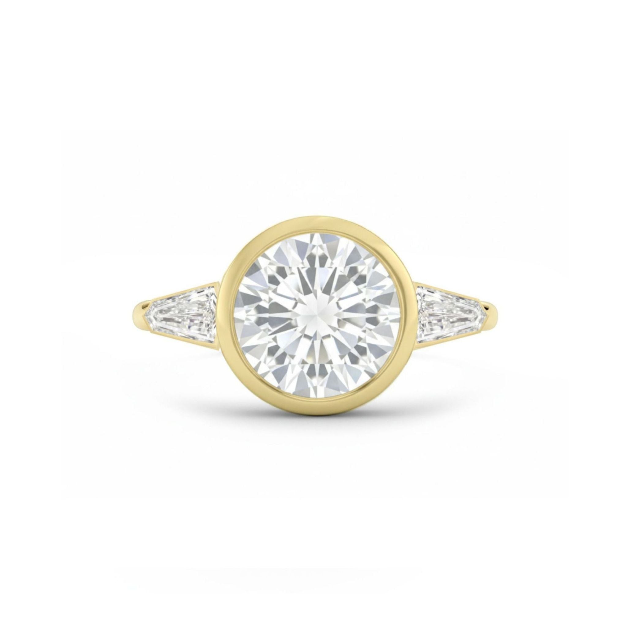 A Bezel Set Round Diamond Engagement Ring with Tapered Baguette Side Stones in Yellow Gold is displayed against a white background, featuring a central large round diamond flanked by two tapered baguette diamonds on each side.