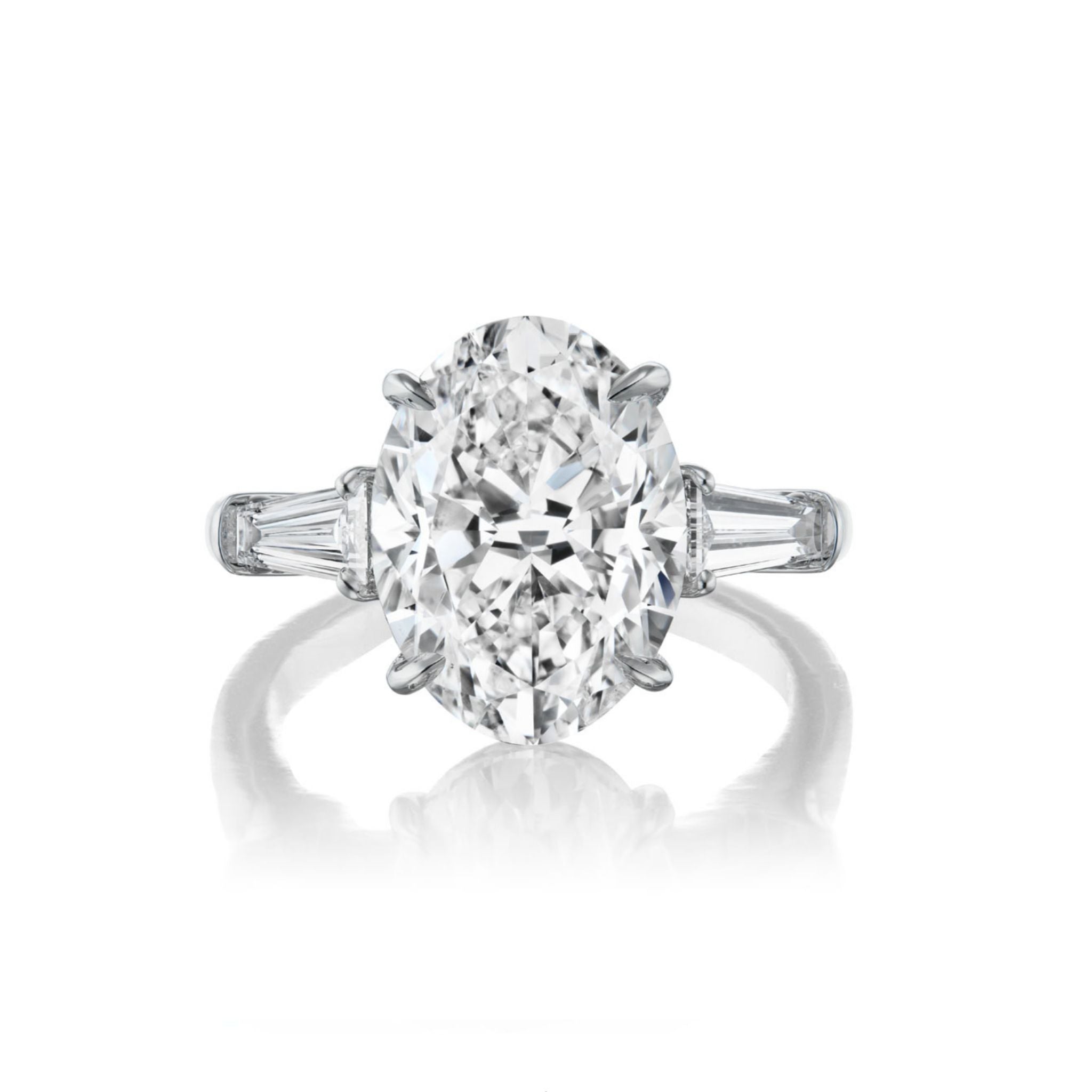 The Oval Diamond Engagement Ring with Tapered Baguette Side Stones, crafted in white gold or platinum and featuring an oval diamond center flanked by two tapered baguette diamonds on each side, is photographed on a white background.