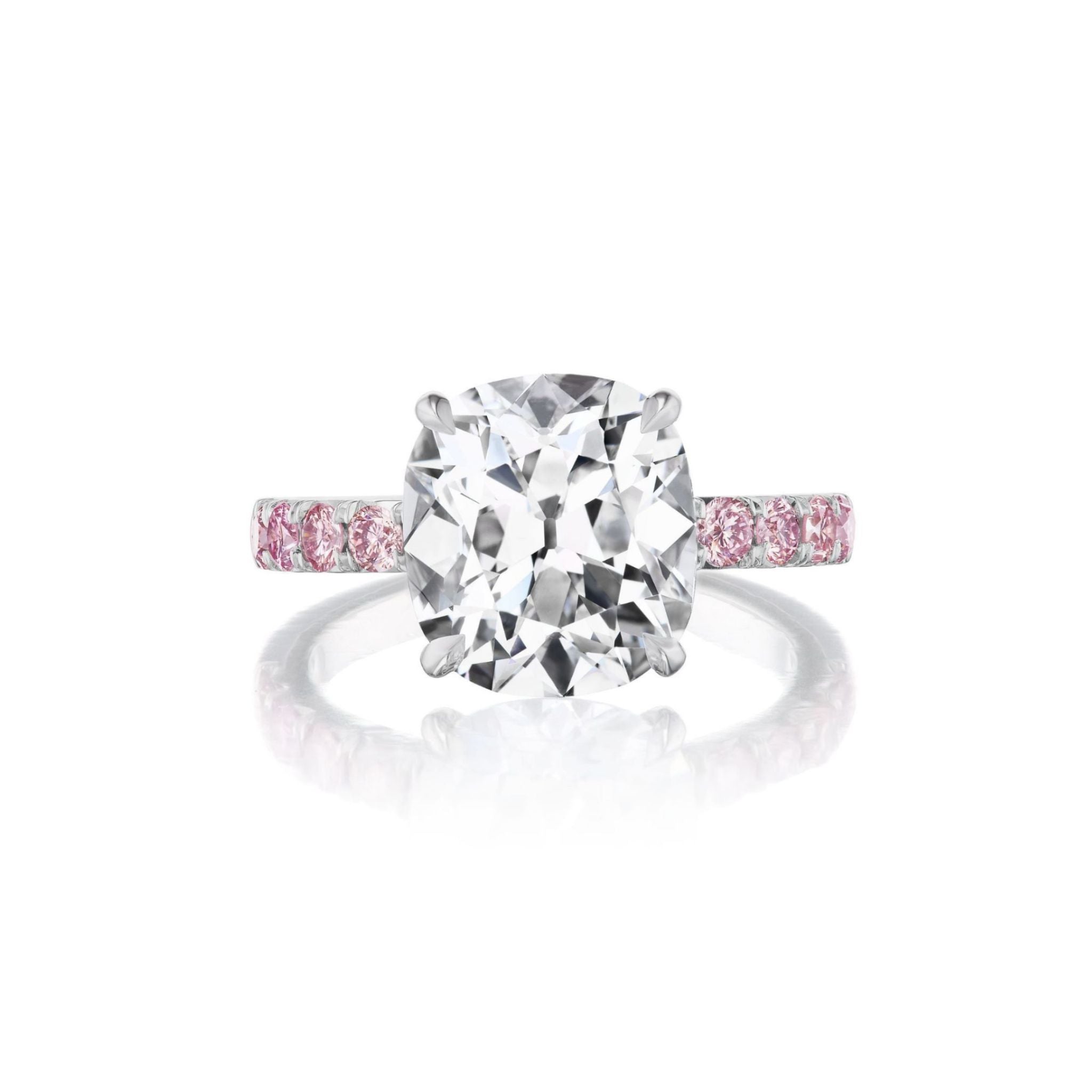 The Cushion Cut Diamond Engagement Ring with Pink Sapphire Pavé Band features a striking cushion cut diamond at the center, set in platinum with delicate pink sapphires embedded along the band, displayed on a white background.