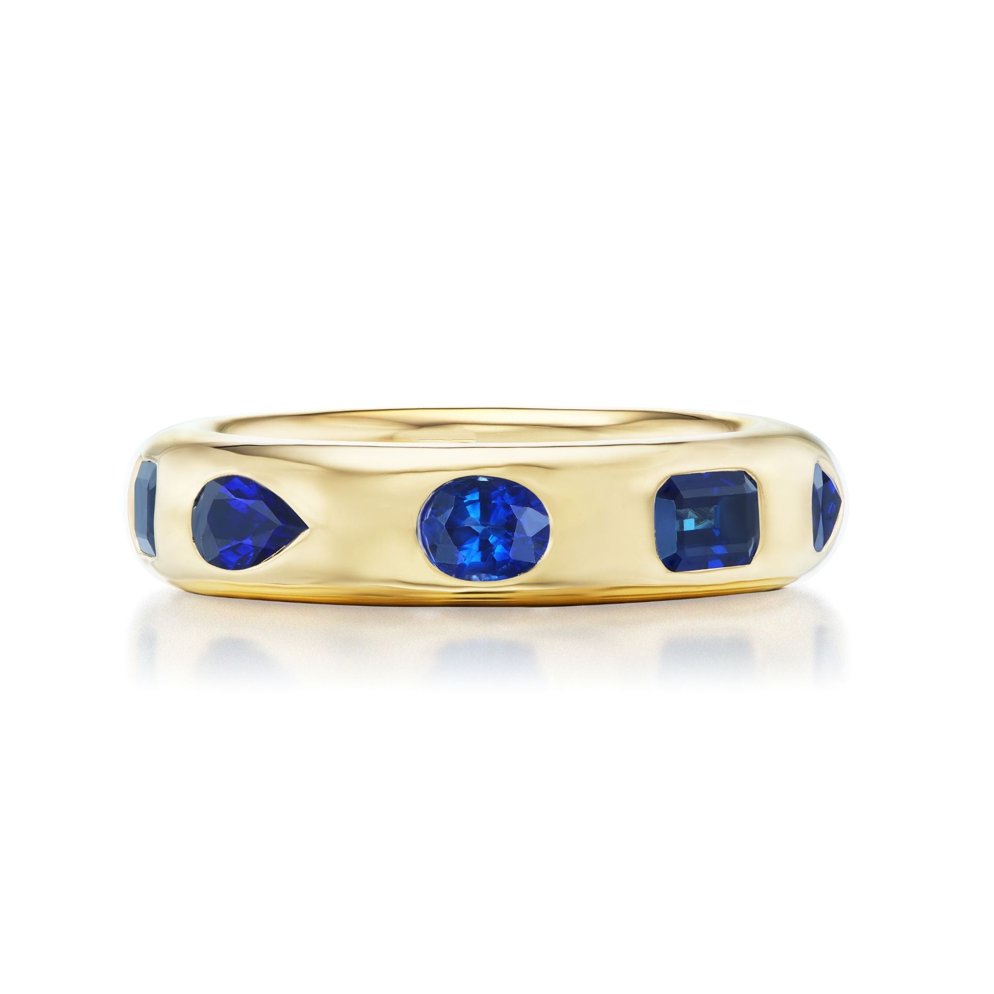 The Wedding Band in Yellow Gold with Burnish Set Mixed Shape Sapphires features blue sapphires in round, square, and teardrop cuts evenly set around an 18K gold band, shown against a white background.
