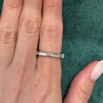 A hand wears the East-West Thin Baguette Cut Diamond Eternity Band, featuring rectangular baguette diamonds set in silver, displayed against textured green fabric. The nails are neatly manicured with a light, natural polish.