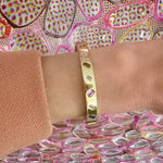 The Mixed Shape Diamond and Multicolor Sapphire Bangle is shown on a wrist in a pink sleeve, with a vibrant background of overlapping pink and yellow shapes.