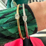 A close-up of a wrist wearing the East-West Oval Solitaire Diamond Bangle in 18K yellow gold and silver, paired with a green and black patterned sweater and a hint of pink garment underneath.