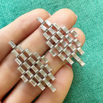 A hand holds Art Deco Chandelier Earrings in white gold, adorned with emerald cut diamonds, displayed against a green textured fabric background.