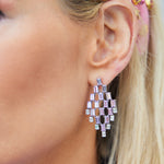Close-up of a woman's ear adorned with Art Deco Chandelier Earrings in white gold, featuring emerald cut diamonds and lavender sapphires. Her blonde hair is tucked behind her ear to showcase the geometric, cascading design.