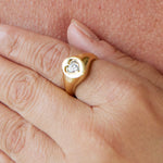 A close-up of a hand wearing the Signet Ring in Yellow Gold with Heart Diamond, the delicate setting resting gently on another person's skin.