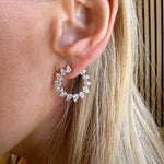 Close-up of a woman with light blonde hair and fair skin wearing the Sunshine Motif Front-to-Back Hoops Small—circular 18k gold earrings accented with multiple clear, pear-shaped diamonds.