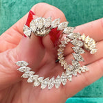 A hand with red-painted nails holds a Jumbo Climbing Ivy Hoop earring in white gold with marquise diamonds, set against a vivid green background.