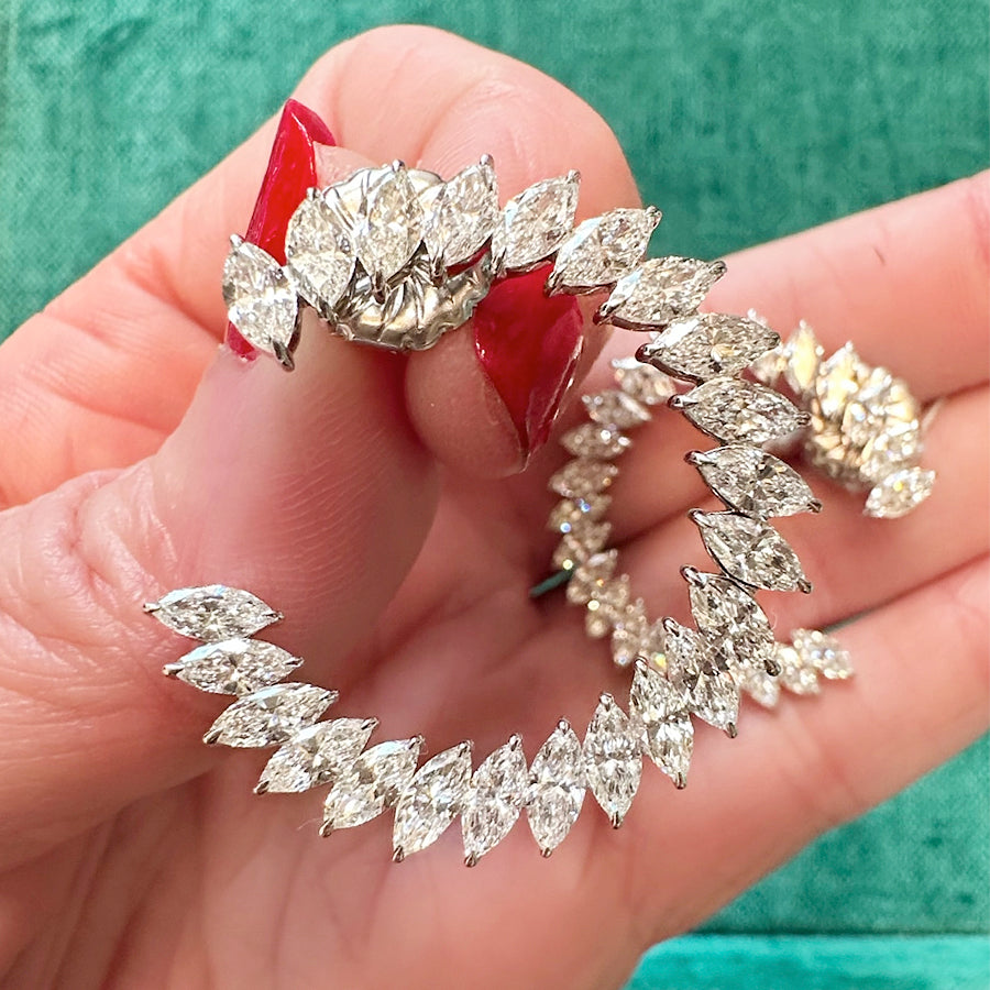 A hand with red-painted nails holds a Jumbo Climbing Ivy Hoop earring in white gold with marquise diamonds, set against a vivid green background.