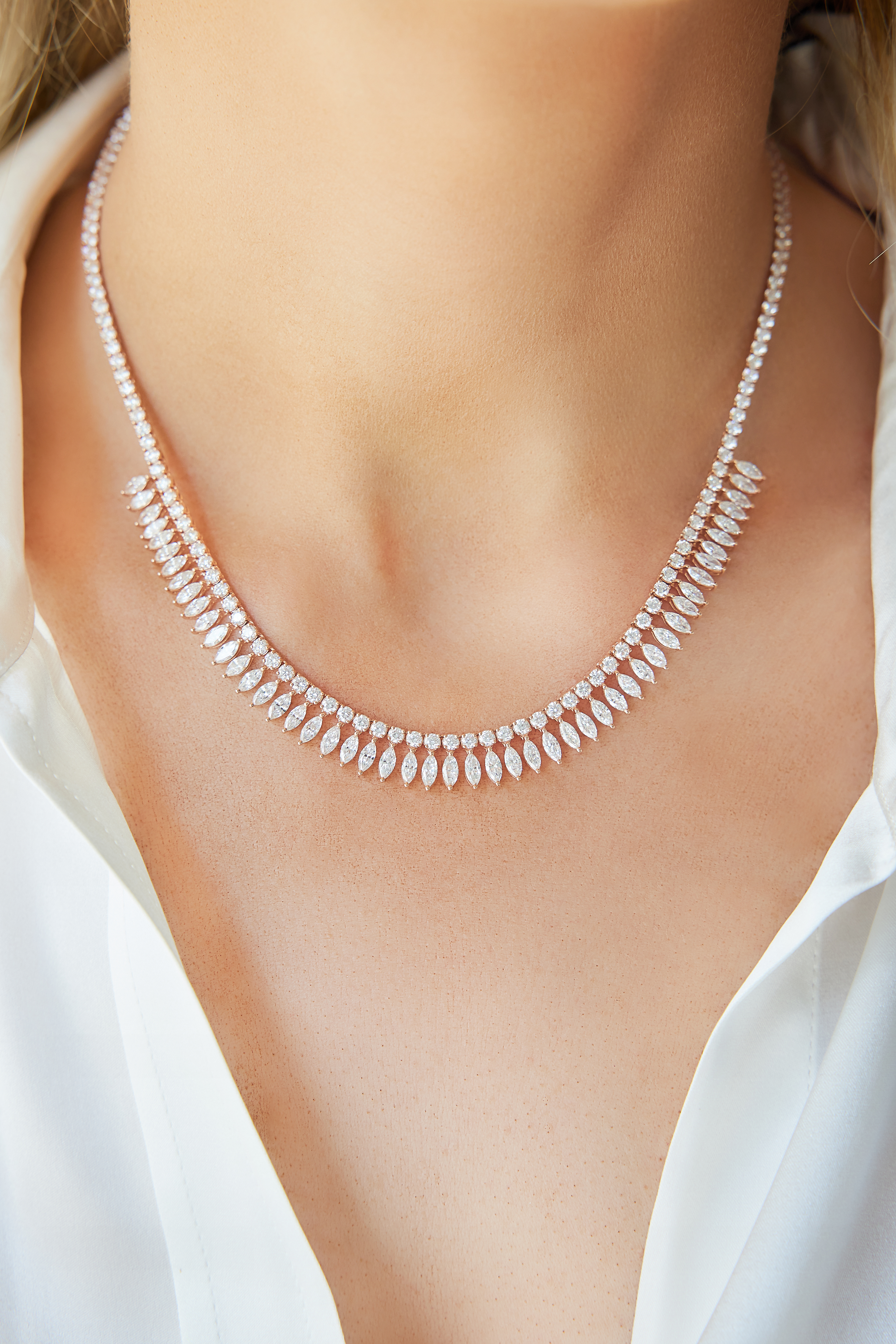 A woman in a white shirt showcases the Deco Feather Collar Necklace with Marquise Diamonds, featuring alternating marquise and round-cut stones in an elegant, symmetrical design and finished with an adjustable chain for a perfect fit.
