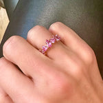 A hand wears the Sapphire Mixed Shape Cluster Ring, crafted from 18K gold and set with five mixed shape pink sapphires, shown against a dark background.