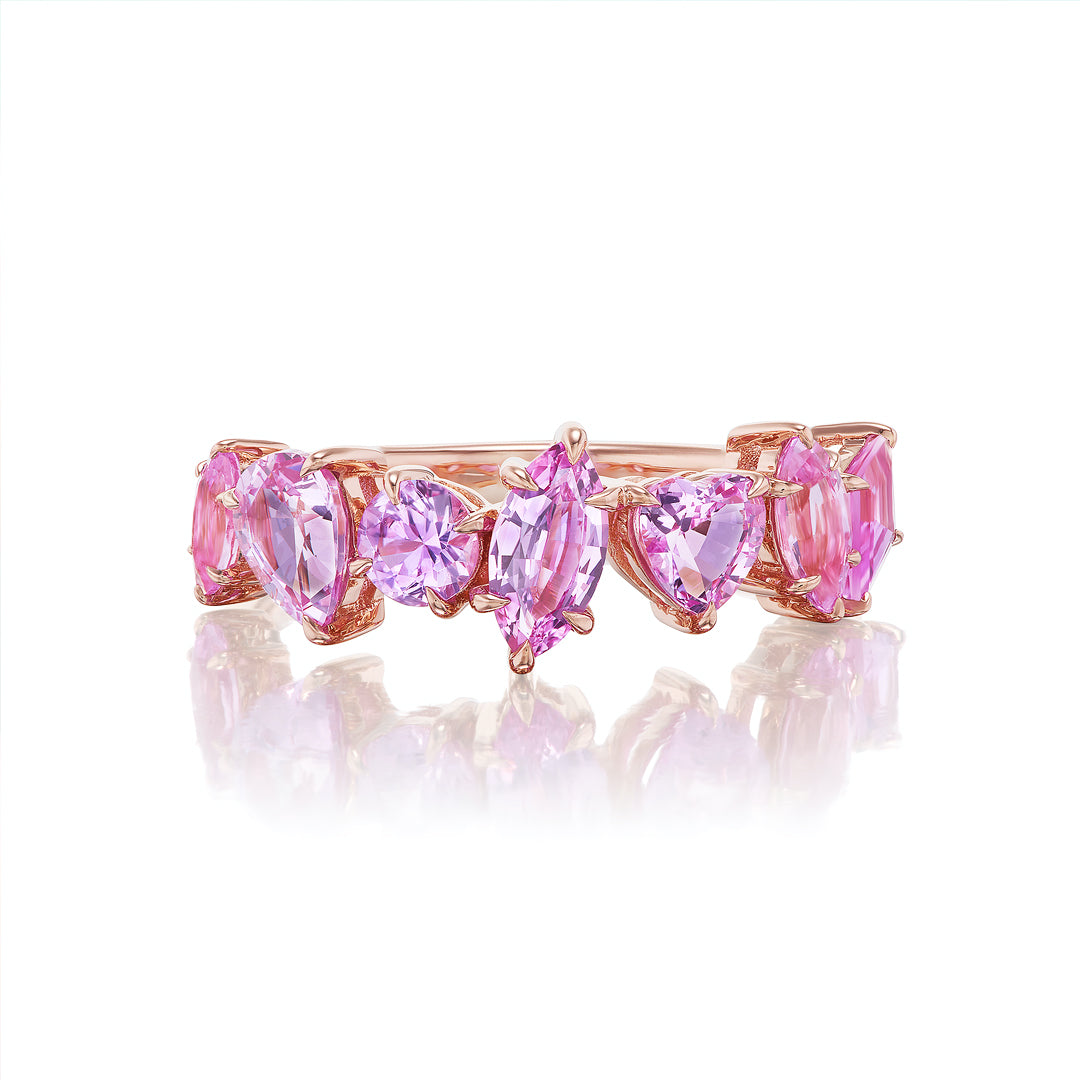 The Sapphire Mixed Shape Cluster Ring is an 18K gold half eternity band with pink and purple sapphires in oval, heart, and marquise cuts, creating a vibrant row set against a white background.