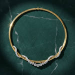 The Coil Graduated Round Diamond and Omega Chain Necklace in Yellow Gold and Platinum is displayed on a dark green marble surface under soft lighting, showcasing its curved, diamond-encrusted design.