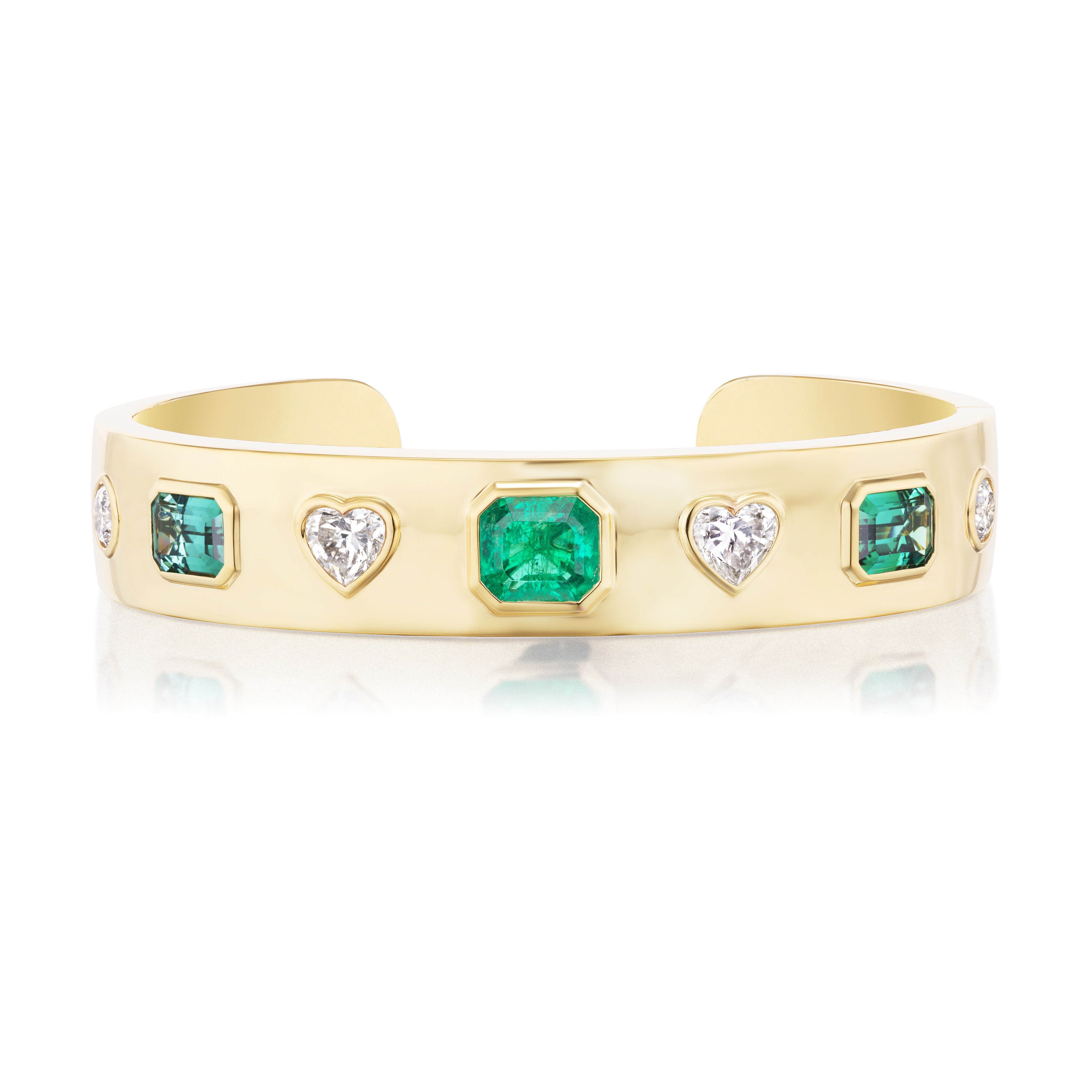 The Bezel Set Mixed Shape Diamond and Emerald Bangle in Yellow Gold features alternating emerald cut emeralds and heart shape diamonds set in a polished 18K yellow gold band.